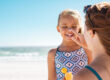 Young mother applying protective sunscreen on daughter nose